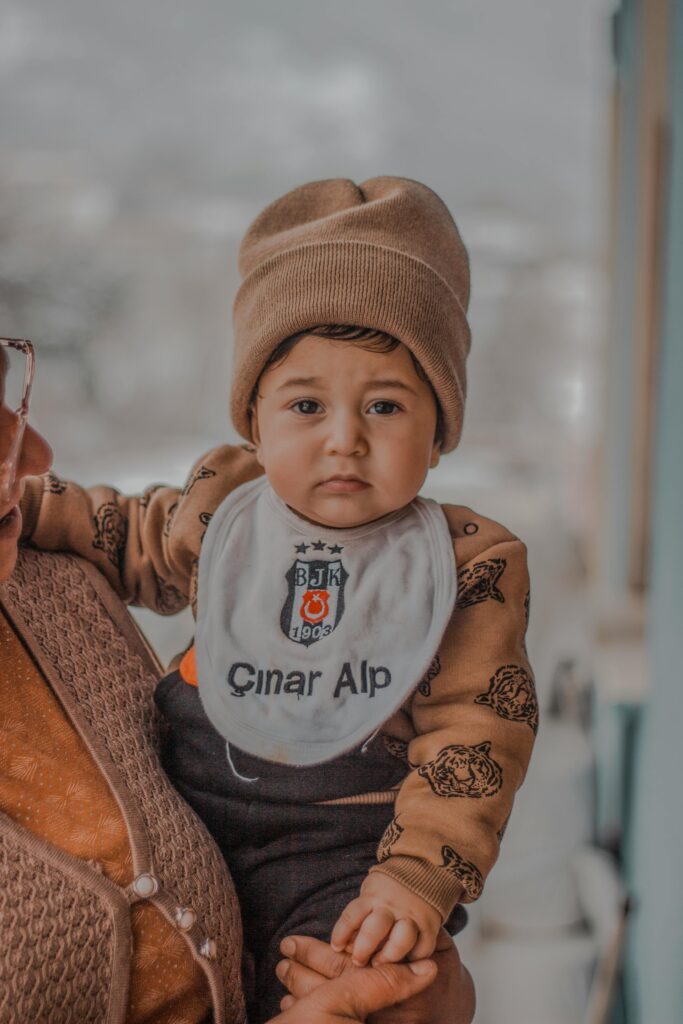 Cute baby boy wearing a beanie and personalized bib, reclining in arms