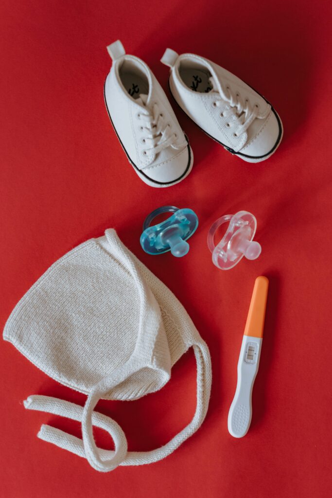 A flat lay of baby shoes, pacifiers, and a pregnancy test on a red background.